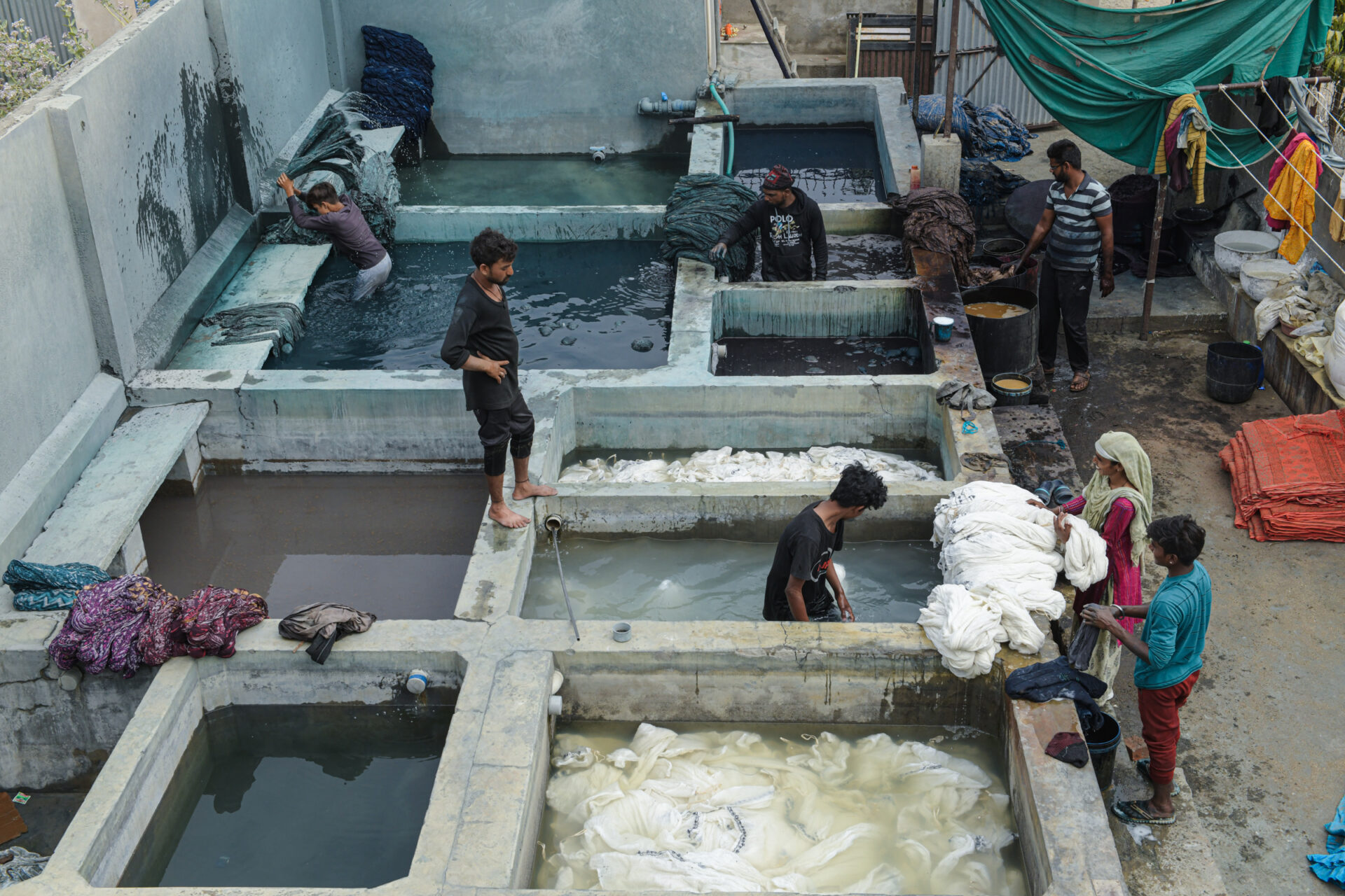 Artisans work in a traditional block printing workshop in India, soaking and dyeing fabrics in large vats and water baths. Block printing and dyeing involve multiple steps, including preparing the cloth, printing and dyeing it with various colours, washing it, and ensuring the dye is set. Each stage requires meticulous attention and skill, highlighting the artisans' dedication and expertise. This vibrant and labour-intensive craft is integral to India's rich textile heritage. Photo Lizane Louw