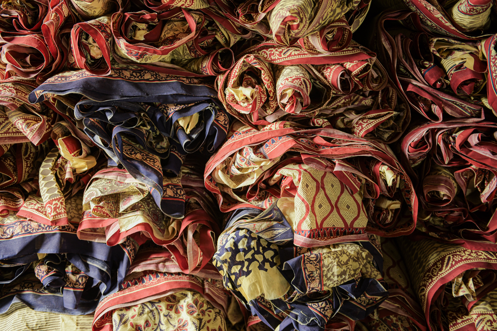 Rolls of intricately patterned and vibrantly coloured block-printed fabrics are stacked in a workshop in India. These textiles, featuring traditional designs and rich hues, represent the artistry and heritage of block printing. Each piece represents the culmination of meticulous craftsmanship, from carving the blocks to applying the inks and dye to the finished product. Photo Lizane Louw