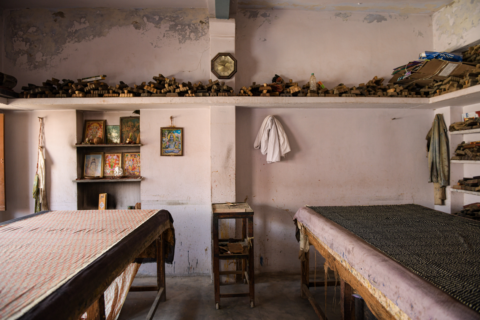 Inside a traditional block printing workshop in India, shelves lined with intricately carved wooden blocks for printing patterns onto fabric. The room, adorned with images of Hindu deities, reflects the craft's cultural and spiritual significance. This space highlights the enduring heritage and skilled craftsmanship that define India's well-known and respected textile industry. Photo Lizane Louw