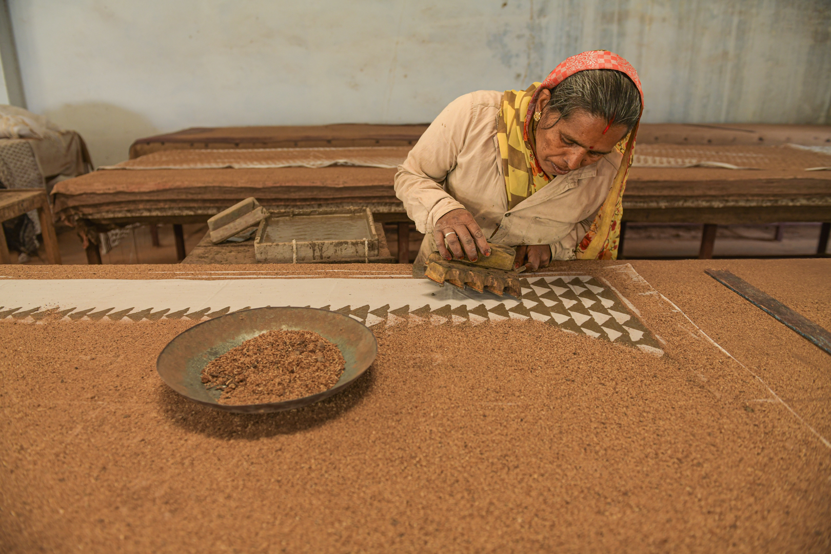 A master printer and seasoned artisan carefully applies a wooden block to fabric, creating intricate geometric patterns in a traditional block printing workshop in India. She demonstrates the precision and skill required for the ancient craft of Dabu, printing with a steady hand and keen attention to detail. Photo Lizane Louw