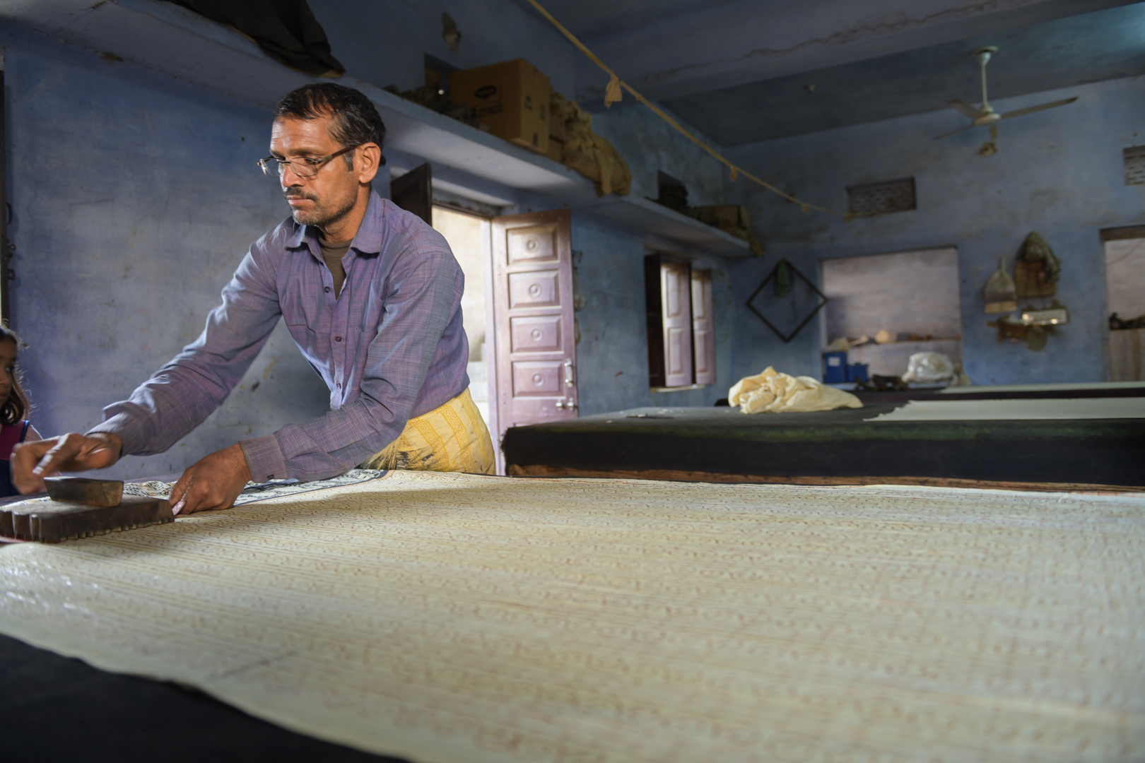 A master printer carefully applies a wooden block to a length of fabric in a traditional block printing workshop in India. The serene, blue-walled workspace reflects the beautiful and visual nature of the craft. The artisans align each print with precision. He is skilled in creating the intricate patterns that characterise this ancient textile art form. Knowledge is passed down through generations and is a craft that is still thriving today. Photo Lizane Louw